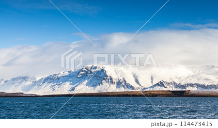 Coastal Icelandic landscape with snowy mountains under dramatic blue sky Coastal Icelandic landscape with snowy mountains under dramatic blue sky 114473415