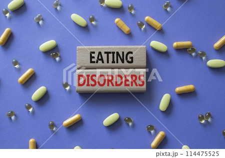 Eating Disorders symbol. Concept word. Eating Disorders on wooden blocks. Beautiful purple background with pills. Medicine and Eating Disorders concept. Copy space 114475525