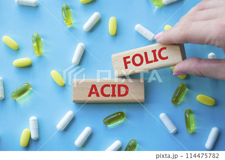 Folic acid symbol. Wooden blocks with words Folic acid. Beautiful blue background with pills. Doctor hand. Medicine and Folic acid concept. Copy space. 114475782