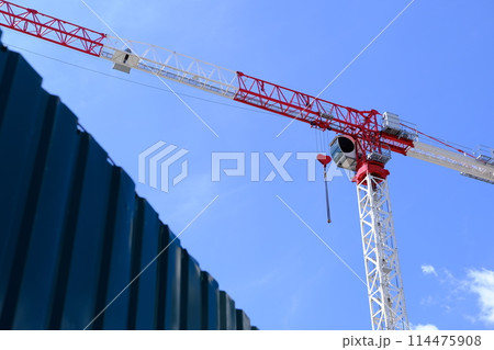 Red and white crane with heart-shaped hook against blue sky. Romantic crane, love-themed equipment, construction site, Valentine's Day concept. 114475908