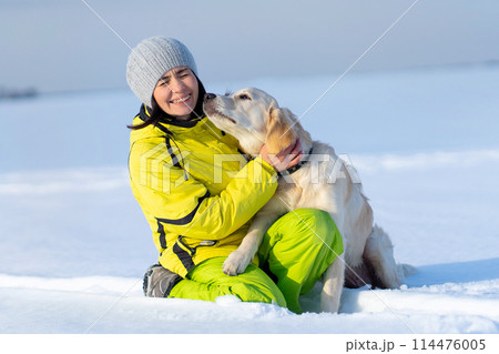 Cute young retriever dog kissing laughing woman on snowy field Cute young retriever dog kissing laughing woman on snowy field 114476005