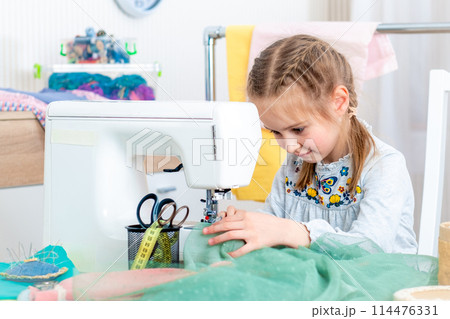 Little girl using sewing machine to make crafts in the workshop 114476331