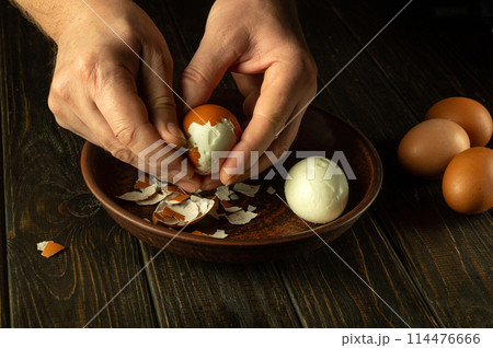 Hands peel an egg. Chef hands peeling boiled eggs on the kitchen table before preparing breakfast Hands peel an egg. Chef hands peeling boiled eggs on the kitchen table before preparing breakfast 114476666