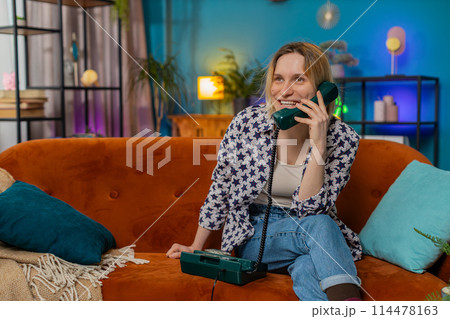 Smiling young woman making wired telephone call conversation with friends sitting on home couch Smiling young woman making wired telephone call conversation with friends sitting on home couch 114478163