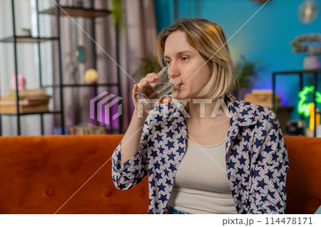 Satisfied Caucasian woman sitting at home on couch leading healthy lifestyle drinking pure water 114478171
