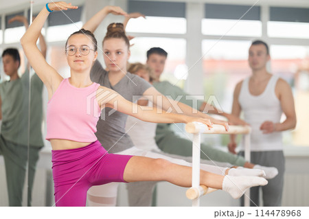 Teen ballet students prepare for classes, near ballet bare stretch legs under man teacher guidance Teen ballet students prepare for classes, near ballet bare stretch legs under man teacher guidance 114478968