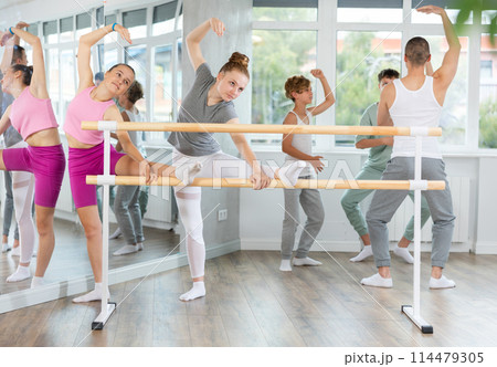 Teen ballet students prepare for classes, near ballet bare stretch legs under man teacher guidance 114479305