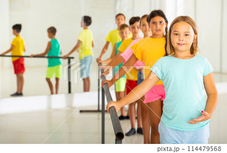 Cheerful girl working near ballet barre during group choreography class Cheerful girl working near ballet barre during group choreography class 114479568