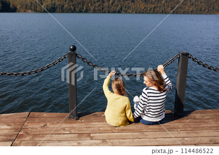 rear view mother and daughter sitting on pier warm autumn day 114486522