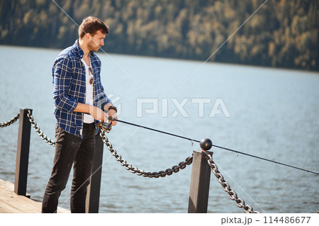 Fisherman standing on riverside and trying to catch fish Fisherman standing on riverside and trying to catch fish 114486677