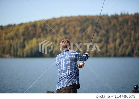 Fisherman standing on riverside and trying to catch fish 114486679