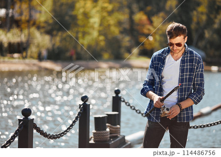 young fisherman with rod and sunglasses fishing in lake young fisherman with rod and sunglasses fishing in lake 114486756