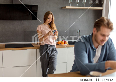 cunny woman is checking her husband's phone while he working at the laptop 114487542