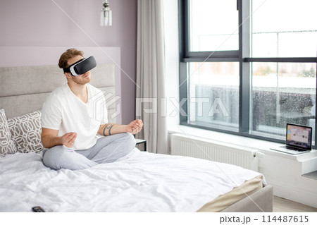 pleasant man in VR headset sitting in yoga pose on the bed pleasant man in VR headset sitting in yoga pose on the bed 114487615