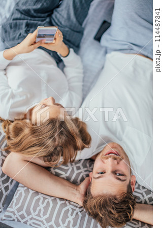 attractive positive guy is looking at the camera while his girl using smartphone 114487841