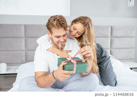 beautiful wife helping to open the gift box to her handsome happy husband 114488638