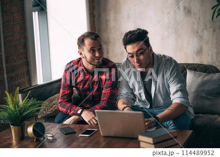 European gay male couple spend time together drinking coffee and watching laptop European gay male couple spend time together drinking coffee and watching laptop 114489952