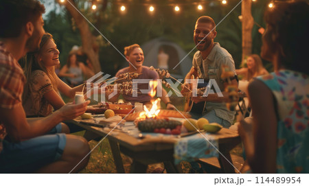 A group of friends enjoy an outdoor barbecue and guitar playing. Camping party A group of friends enjoy an outdoor barbecue and guitar playing. Camping party 114489954