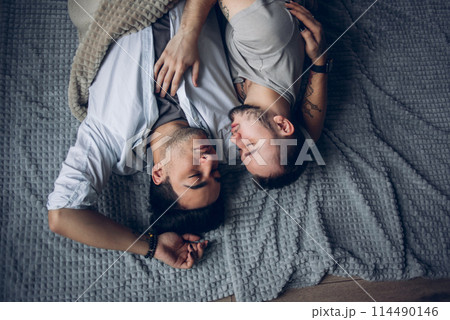 Handsome sleepy man with bristle kissing good night male partner lying in bed 114490146