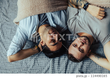 Handsome sleepy man with bristle kissing good night male partner lying in bed 114490165