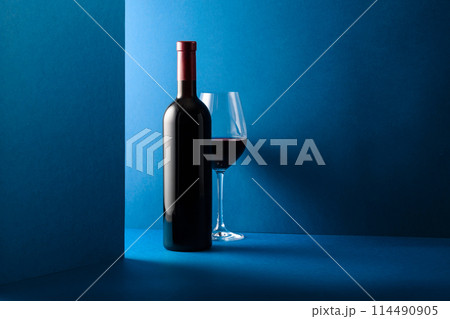Bottle and glass of red wine on a blue background. Bottle and glass of red wine on a blue background. 114490905
