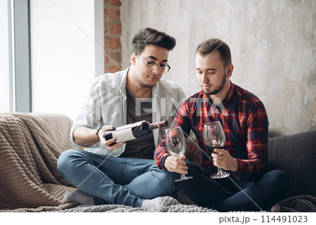 Laughing male gay couple drinking wine and preparing a meal 114491023