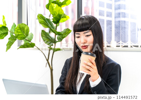 コーヒーを飲みながら仕事をする女性社員 コーヒーを飲みながら仕事をする女性社員 114491572