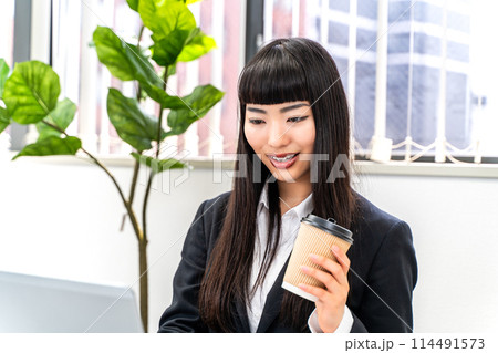 コーヒーを飲みながら仕事をする女性社員 コーヒーを飲みながら仕事をする女性社員 114491573
