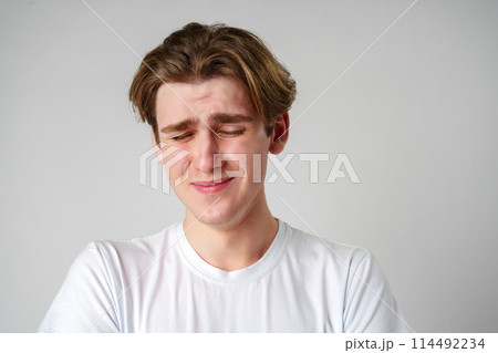 Young Man With Brown Hair Expressing Sadness Against a Plain Background Young Man With Brown Hair Expressing Sadness Against a Plain Background 114492234