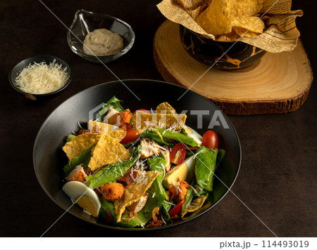 On dark background, delicious Mexican Nacho salad bowl is beautifully garnished with tortilla chips, boiled eggs, and fresh vegetables On dark background, delicious Mexican Nacho salad bowl is beautifully garnished with tortilla chips, boiled eggs, and fresh vegetables 114493019