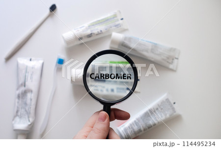 Dangerous toothpaste ingredient carbomer. Checking the composition of toothpaste with a magnifying glass against the background of many tubes 114495234