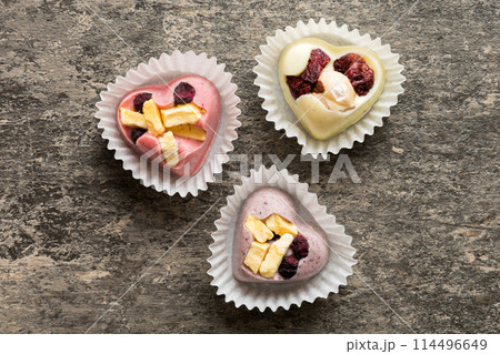 chocolate sweets in the form of a heart with fruits and nuts on a colored background. top view with space for text, holiday concept chocolate sweets in the form of a heart with fruits and nuts on a colored background. top view with space for text, holiday concept 114496649