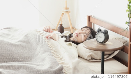 目覚まし時計をセットして寝る女性 114497805