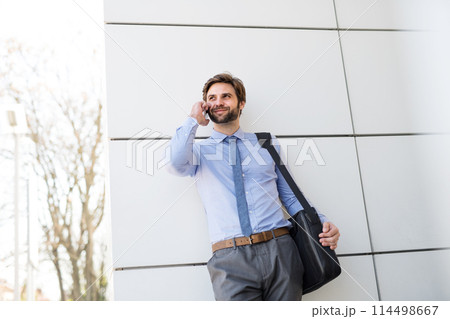 Handsome businessman phone calling on smartphone while walking on city street, going to office. Manager smiling, outdoor in urban setting Handsome businessman phone calling on smartphone while walking on city street, going to office. Manager smiling, outdoor in urban setting 114498667