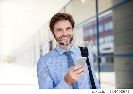 Handsome businessman scrolling on smartphone while walking on city street, going to office. Manager smiling, outdoor in urban setting Handsome businessman scrolling on smartphone while walking on city street, going to office. Manager smiling, outdoor in urban setting 114498671