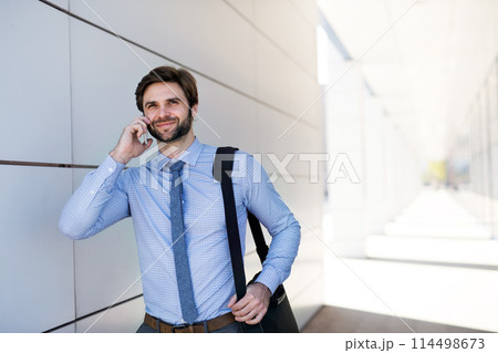 Handsome businessman phone calling on smartphone while walking on city street, going to office. Manager smiling, outdoor in urban setting Handsome businessman phone calling on smartphone while walking on city street, going to office. Manager smiling, outdoor in urban setting 114498673