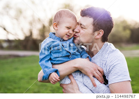 Father holding little toddler boy kissing him, making him laugh, having fun during warm spring day. Father's day concept. Father holding little toddler boy kissing him, making him laugh, having fun during warm spring day. Father's day concept. 114498767