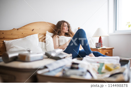 Beautiful woman lying on bed next to packed suitcase. Solo traveller preparing for trip. Beautiful woman lying on bed next to packed suitcase. Solo traveller preparing for trip. 114498878
