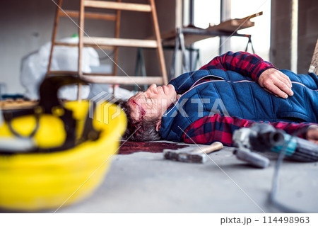 An unconscious man worker lying on the floor after a head injury. Work injury, accident in workplace. An unconscious man worker lying on the floor after a head injury. Work injury, accident in workplace. 114498963