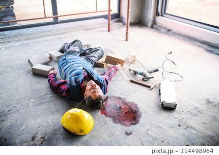 An unconscious man worker lying on the floor after a head injury. Work injury, accident in workplace. An unconscious man worker lying on the floor after a head injury. Work injury, accident in workplace. 114498964