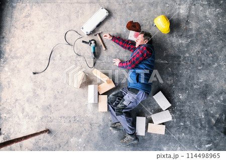 An unconscious man worker lying on the floor after a head injury. Work injury, accident in workplace. 114498965