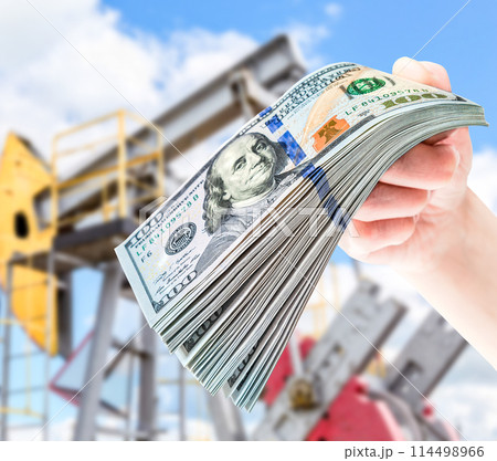 American dollars in the hand against the oil pump jack extraction machine American dollars in the hand against the oil pump jack extraction machine 114498966