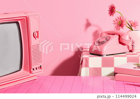 Pink concept photo with frontal shot, a television with pink color, a pink desk phone placed on the back table with a flower vase next to it. Vacant space on pink table for showing product 114499024
