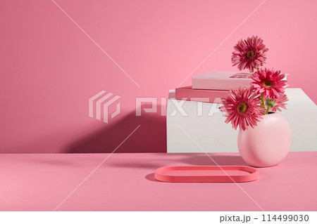 Over pink background, an blank tray with pink color placed next to a flower vase on pink table. Frontal shot photo with blank space for displaying product with pink tone 114499030