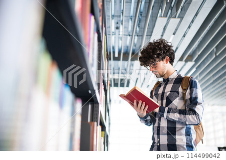 Male student in library, looking for books, preparing for final exam. 114499042