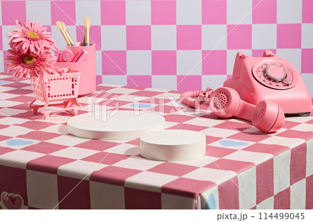Creative photography with checkered pattern, empty white pedestals placed on table surrounded by some accessories for daily life and gerbera daisy decoration. Blank space for design 114499045