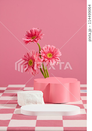 Creative design template of gerbera flower theme in pink tones, white blank tray placed in front with an empty flower shaped pedestal in back. Copy space for text, front view 114499064