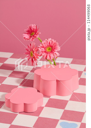 High angle shot at two pedestal in flower shaped displayed on pink checkered tablecloth with flor gerbera daisy decoration. Vertical photo for promotion with blank space for showing product 114499068