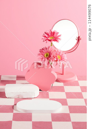 Vertical photo in pink and white tone, an empty tray placed in front, some pedestal, a mirror and gerbera flowers featured in back. Space for presentation, front view 114499076
