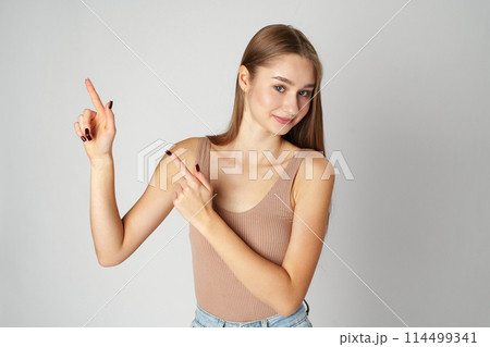Young Woman in Tank Top Pointing at Something on gray background Young Woman in Tank Top Pointing at Something on gray background 114499341